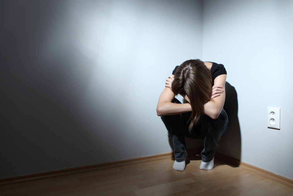 woman sitting in a dark corner with her head down