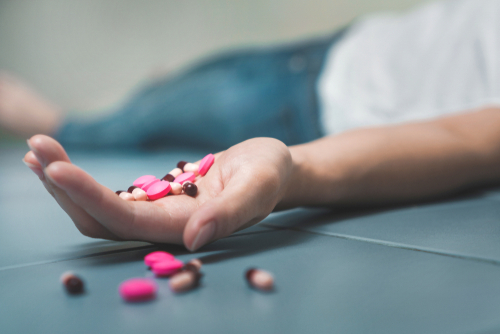 person laying on floor with a bunch of pills in their hand