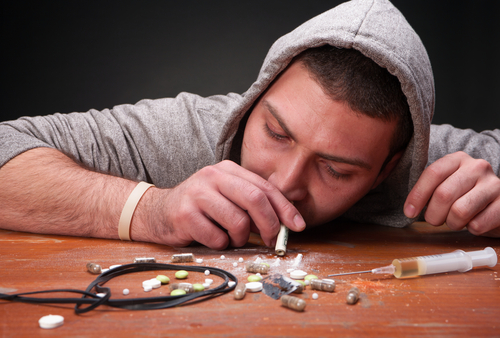 man snorting pills with other various drugs around him
