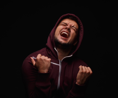 man yelling while using a syringe to get high