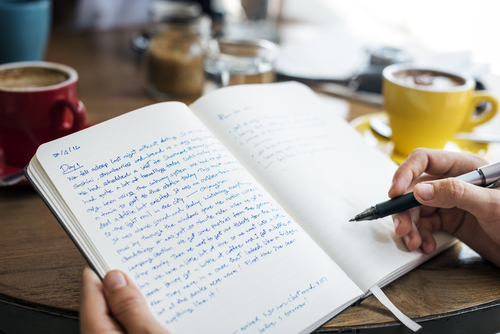 person writing in a journal with things already wrote in the journal