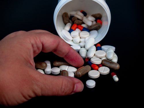 hand reading into spilled pill bottle, grabbing many different types of pills