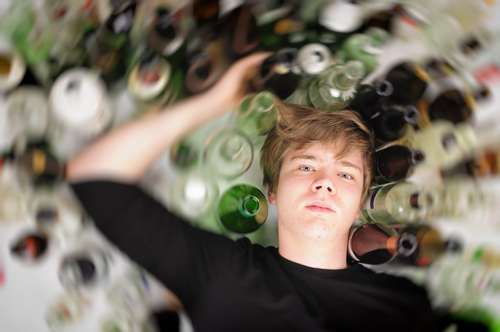 man laying down with lots of alcohol bottles around him