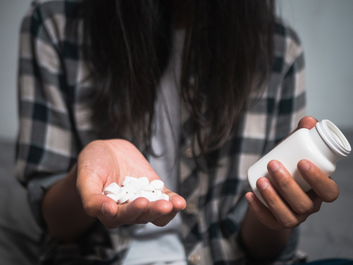 person holding a bunch of pills in one hand and the pill bottle in the other