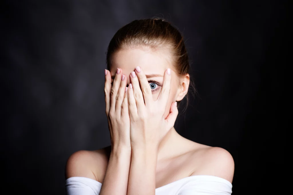woman with her hands over her eyes and peaking out in between her fingers